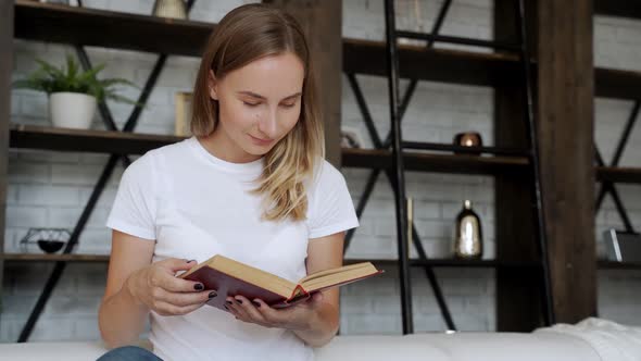 Beautiful Young Woman Reading a Book on the Sofa