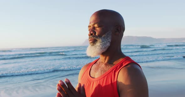 Senior african american man practising yoga with eyes closed at the beach