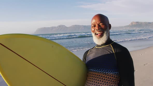 Smiling senior african american man walking with a surfboard at the beach