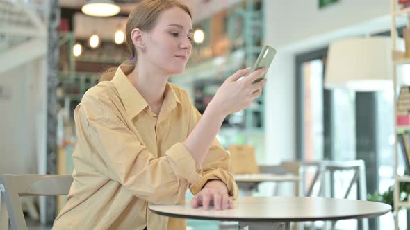 Young Woman Scrolling on Smartphone in Cafe 