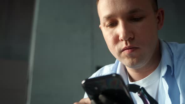 Concentrated man in blue shirt types on smartphone holding device