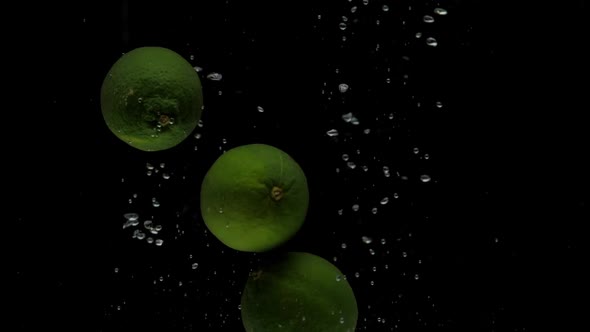 Slow Motion Three Lime Falling Into Transparent Water on Black Background