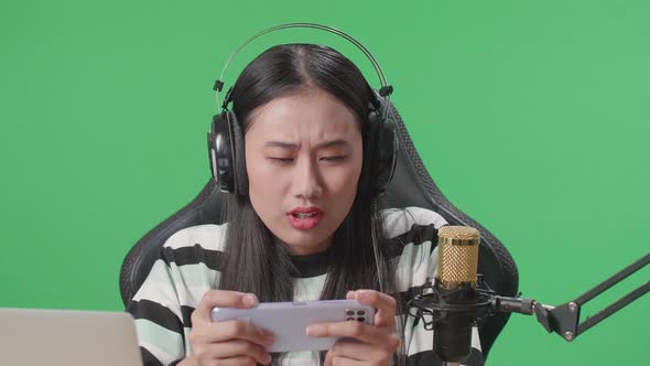 Upset Asian Woman Gamer With Headphone Losing Mobile Phone Game On The Green Screen Background