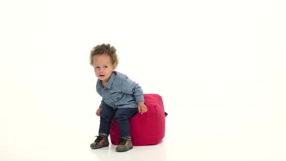 Little African American Boy Sits on a Pillow in the Studio. White Background. Slow Motion