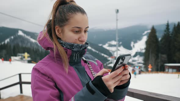 Young Beautiful Woman Uses a Mobile Phone on the Lift of a Ski Resort Mountains and Skiers in the