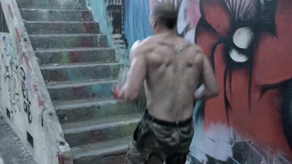 A shirtless personal trainer man carries a concrete block up stairs