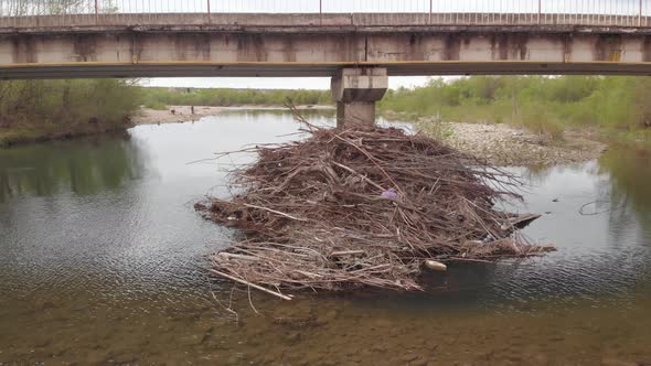 Debris Branches Wood and Rubbish Litter Pile Up Against Bridge Pillar at the River in Ukraine in