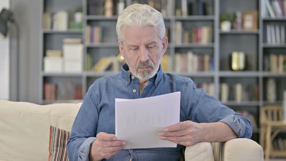 Old Man Reading Documents on Sofa