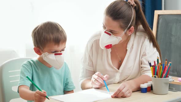 Little Boy Wearing Medical Mask Respirator Drawing or Writing on Paper While Doing Homework with His