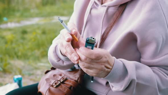 Woman Holding a Cigarette and a Lighter in Hands While Sitting in Nature on Sun