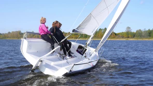 A Guy and Two Girls Demonstrate a Turn on a Sail Boat By Controlling the Sail with Their Feet and