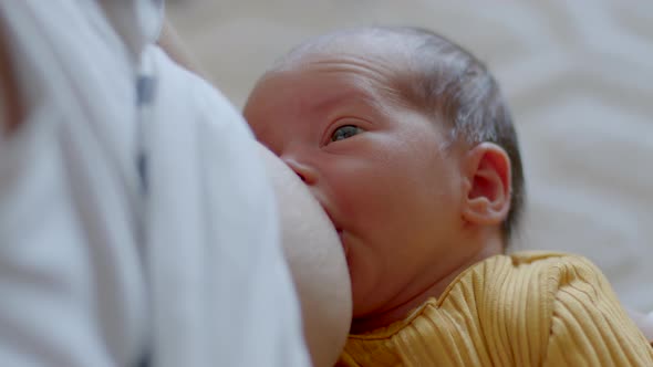 A Newborn Small Baby in Yellow Jumpsuit Eating Milk From the Mother's Breast