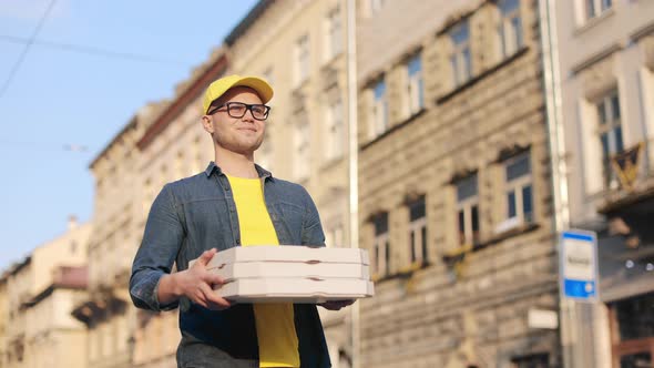 A Young Happy Delivery Man is Going and Holding Three Pizza Boxes