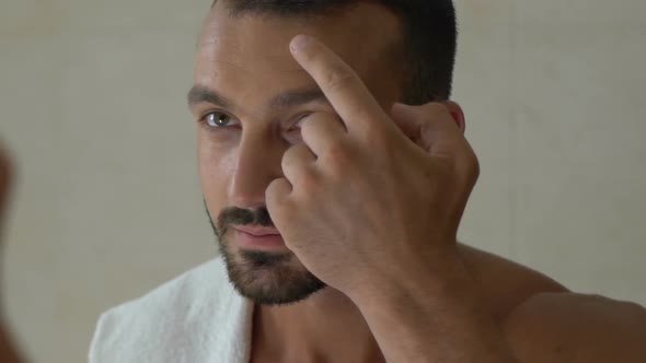 Man Applying Cream on His Face in Front of Mirror in Bathroom, Cosmetics for Men