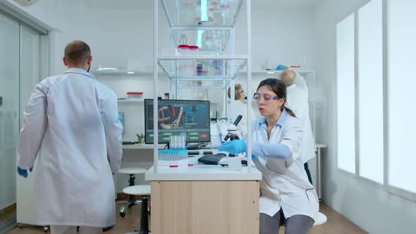 Woman Scientist Examining Petri Dish and Looking Down on Microscope alt