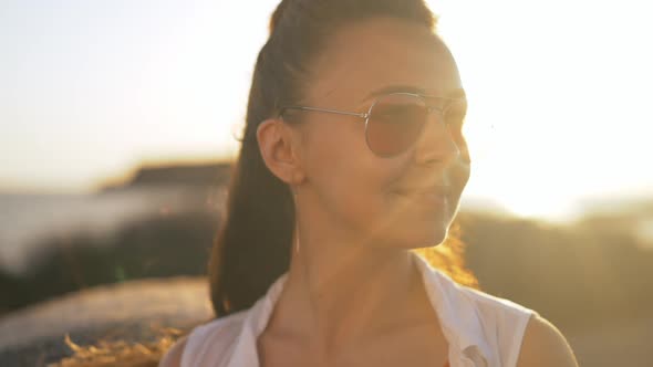 Closeup Portrait of Happy Relaxed Young Woman in Sunglasses Looking Away Standing in Golden Sunrays