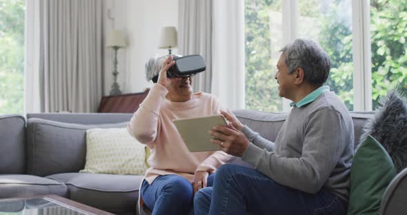 Happy mixed race senior couple wearing vr headset and having fun at home