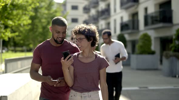 Happy Young Couple Walking on Street and Looking at Smartphone