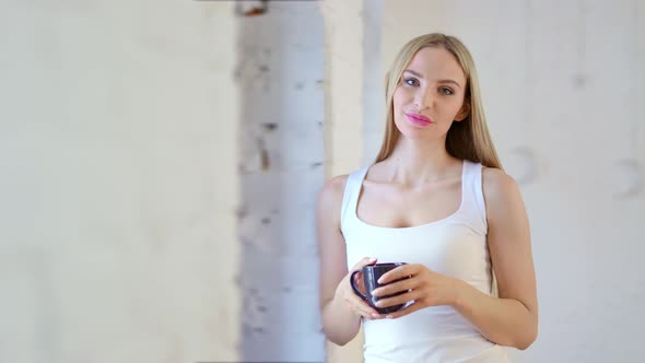 Portrait of Smiling European Woman Holding Mug Standing at Studio or Home White Loft Background