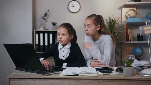 Girls Sitting Together at the Table and Doing Homework Using Computer