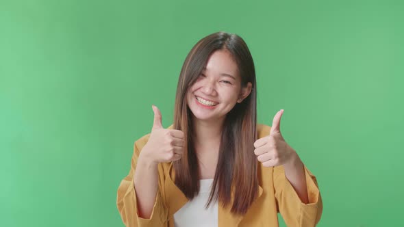 Happy Asian Woman Showing Thumbs Up Gesture While Standing In The Green Screen Studio