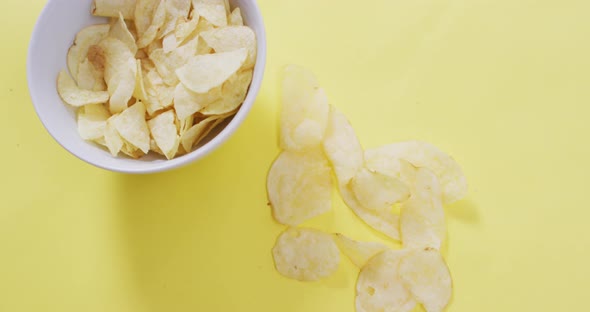 Close up of potato chips falling in a bowl on yellow surface