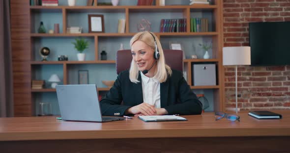 Businesswoman with Headset Holding Videoconference on Laptop with Colleagues