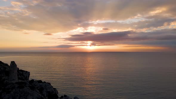 Aerial shot zoom in movement of a sunrise with some clouds and sun rays in the Mediterranean sea.