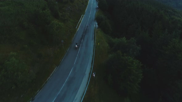 Top View of Man Riding Motorcycle on Winding Mountain Pass with Forested Hills at Sundown