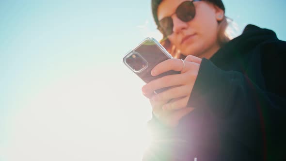 An Attractive Young Woman in Sunglasses Texting on Her Phone