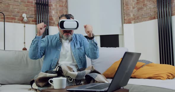 Man in Virtual Reality Headset Watching Video Match and Rejoicing the Getted Results with Hands Up