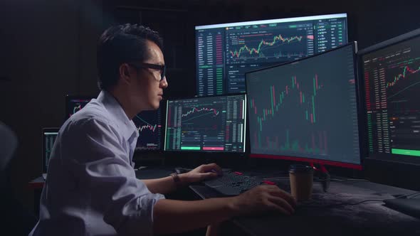 Side View Of A Asian Young Male Stock Market Broker Analyzing Graphs On Multiple Computer Screens