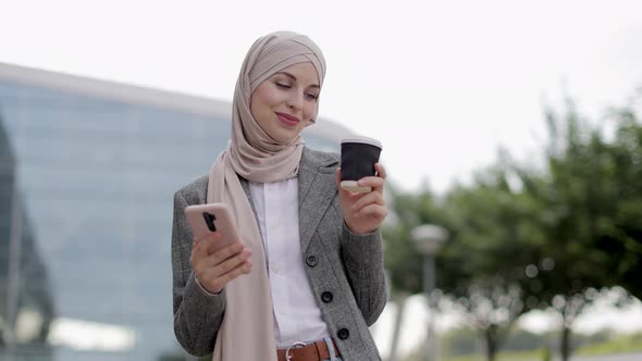 Arab Woman in Headscarf Walking on the Street with Take Away Coffee and Phone