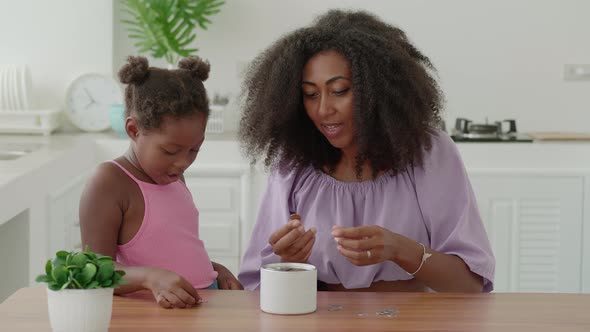 Happy African Family of Two Beautiful Mother and Daughter Count Coins and Throw Them Into the Piggy