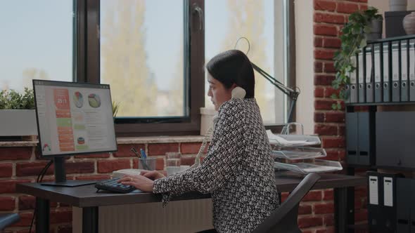 Asian Person Using Office Telephone While She Works on Computer