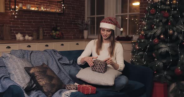 Young Happy Pretty Girl with Christmas Hat Sitting on the Sofa Near Christmas Tree Preparing
