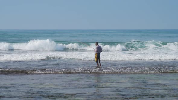 Local Fisherman Holds Rod in Hand in Waving Blue Ocean