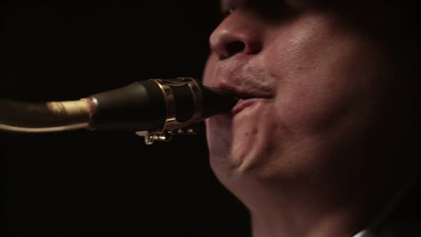 Man Blows Into the Mouthpiece of a Saxophone with Mouth in Darkness Closeup