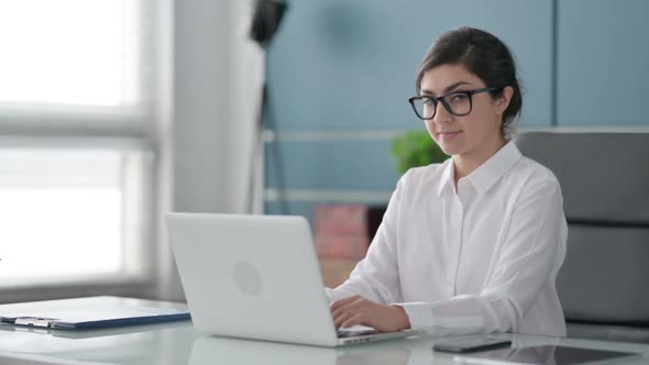 Indian Businesswoman Showing Thumbs Up Sign While using Laptop in Office