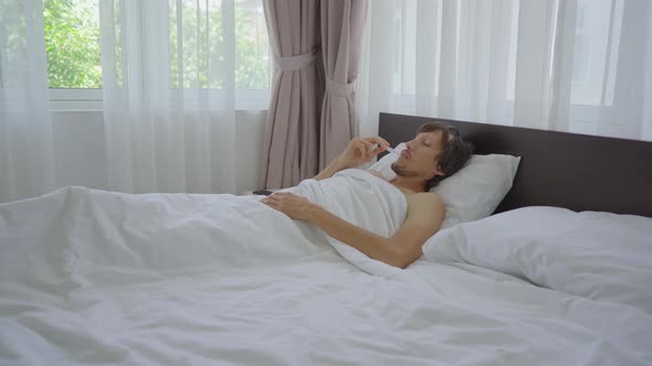 A Young Man in a Bed Puts on a Teeth Guard Before Going To Sleep. Anti Grinding Teeth Protector