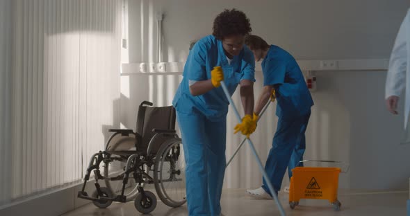 Diverse Janitors Washing Floor in Hospital Room with Empty Wheelchair