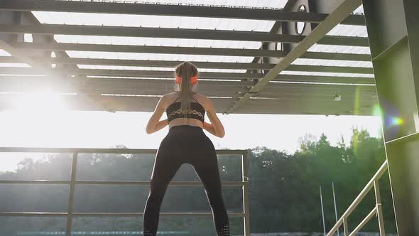 Young Woman in Fitness Clothes which Doing Squat Exercises Outdoors Under Roof