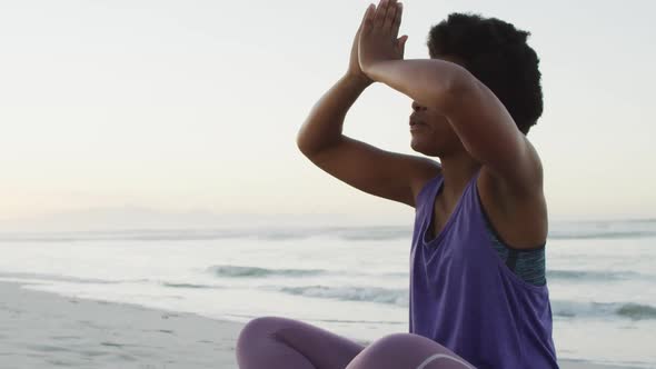 African american woman practicing yoga and meditating on sunny beach