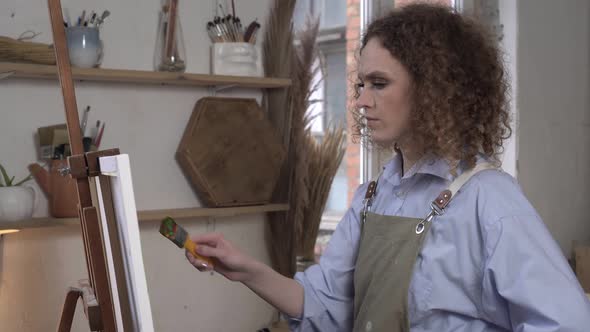 Serious Woman Artist Paints a Picture in a Studio with Concentration