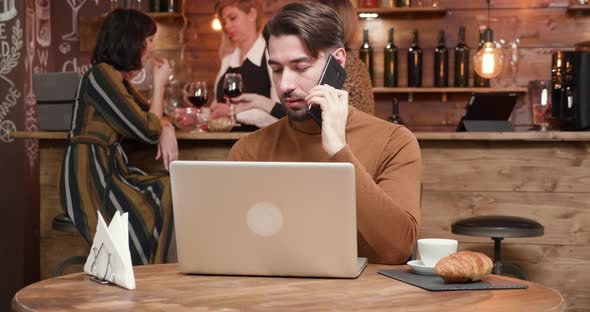 A Handsome Young Businessman Talking on His Phone While Working in a Bar