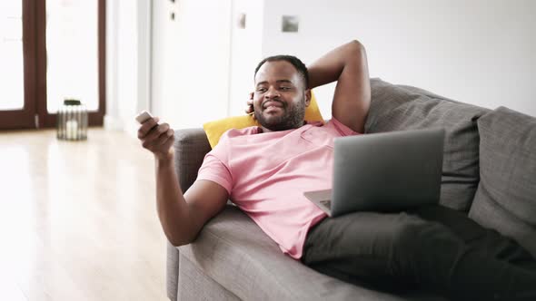 Smiling African man switching channels on TV