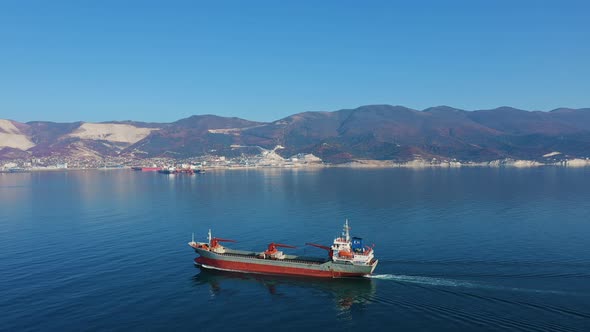 Aerial View Following the Ultra Large Cargo Ship at Sea Leaves Port at Sunny Day