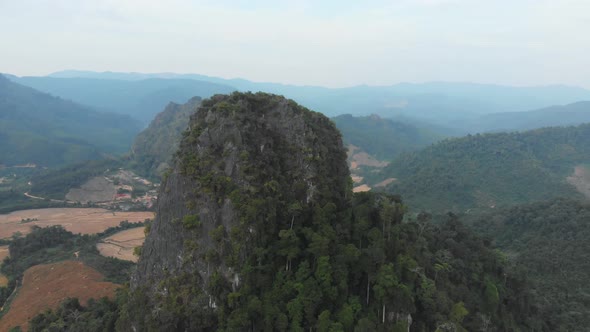 Aerial: flying over rice paddies unique valley scenic cliffs rock pinnacles tropical jungle Laos