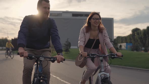 Young Man and His Girlfriend Are Riding Bikes in a City in Summer Evening