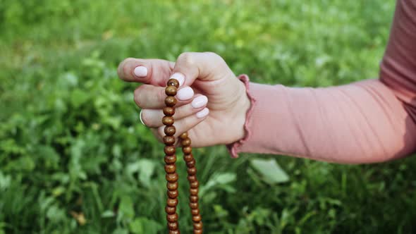 Hand of Young Believing Woman Prays in Nature and Uses Craft Rosary Beads To Count Prayer and alt